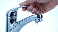 Caucasian male hand turning off chrome kitchen faucet with dripping water drop, water saving and plumbing repair concept.