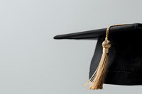 Black graduation cap with gold tassel against neutral gray background, symbolizing academic achievement and educational milestone.