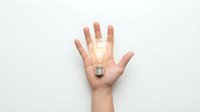 Open hand holding glowing light bulb against white background representing creativity, innovation, bright ideas and inspiration for business concepts.