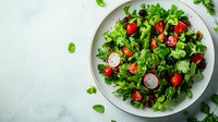 Fresh green salad with cherry tomatoes, sliced radishes and mixed leafy greens served on white ceramic plate against light marble background. Healthy eating concept.