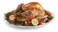 Roasted whole chicken garnished with fresh rosemary sprigs, cherry tomatoes, lemon slices and garlic on white plate, traditional holiday dinner preparation.