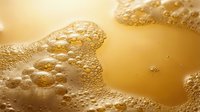 Macro shot of golden liquid with foam bubbles and textured surface, suitable for beverage, cosmetics, skincare, and luxury product advertising.