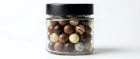 Glass jar filled with assorted chocolate truffles and candy balls in dark, milk, and white varieties, isolated on white background.