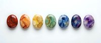 Polished gemstone spheres in rainbow colors arranged in a row on white background, representing chakra healing crystals for wellness and spiritual practices.