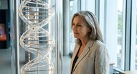 Senior Caucasian female scientist examining DNA double helix model in modern laboratory. Professional researcher studying genetic structure for medical research.