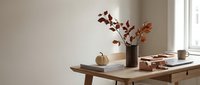Cozy autumn home interior with wooden desk, decorative pumpkin, dried branches in vase, books and warm natural lighting creating peaceful workspace atmosphere.