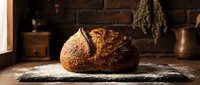 Freshly baked artisan sourdough loaf with crispy crust resting on flour-dusted surface in rustic kitchen setting, ideal for bakery, food, and culinary content.