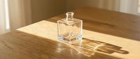 Empty glass perfume bottle with square shape on wooden table with sunlight casting shadow, suitable for fragrance product mockups and cosmetic branding designs.