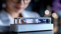 Futuristic levitating display device with glowing purple holographic effects floating above white base against blurred background with bokeh lights.