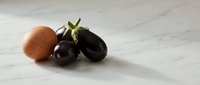 Fresh organic eggplants and brown egg on white marble surface for healthy cooking and farm-to-table cuisine preparation.