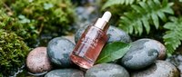 Cosmetic serum bottle with dropper surrounded by smooth stones and green moss, ideal for skincare and beauty product marketing.