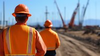 Construction workers in safety gear supervising industrial site with cranes. Professional team wearing hard hats and high-visibility vests for workplace safety.
