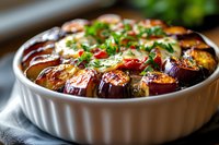 Roasted eggplant slices arranged in ceramic baking dish, topped with fresh herbs, chili flakes and sauce. Close-up view of Mediterranean appetizer.