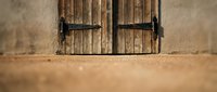 Rustic wooden shutters with iron hinges on weathered stone wall create authentic Mediterranean architectural detail for interior design projects.