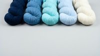 Five yarn skeins in blue gradient from navy to cream arranged on white background for crafting and knitting projects.