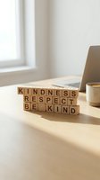 Wooden letter blocks spelling kindness respect be kind on desk with coffee cup and laptop in bright office workspace for motivation and positive mindset concepts.