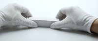 Hands in white protective gloves holding blank gray card on white background. Medical safety equipment for healthcare professionals and laboratory work.