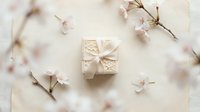 Elegant cream gift box with floral embossing and ribbon bow surrounded by delicate pink cherry blossoms on soft beige background.