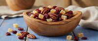 Wooden bowl filled with mixed nuts, dried cranberries and candied ginger pieces on rustic kitchen counter for healthy snacking and cooking ingredients.