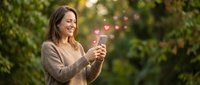 Young woman holding smartphone with floating heart icons in outdoor park setting, social media love concept for dating apps and digital romance communication.