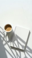 Overhead view of white mug with coffee and blank spiral notebook on white surface with natural shadow, workspace setup for business, creative writing, or planning projects.