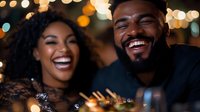 Young African American couple laughing together at night celebration with festive bokeh lights background, sharing authentic joyful moment during romantic date.