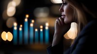 Young blonde woman in contemplative pose against blurred blue candle lights creating atmospheric bokeh effect, side profile in dark moody setting.