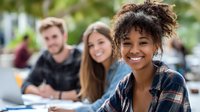 Diverse group of college students studying outdoors, with focus on smiling young woman with natural curly hair in plaid shirt.