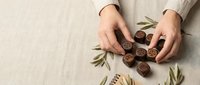 Hands holding artisan chocolate truffles with olive branch decoration on natural linen background for gourmet food photography and luxury confectionery marketing.