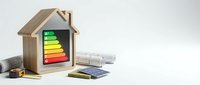 Wooden house model with energy efficiency rating chart and architectural blueprints for sustainable building design and eco-friendly construction planning.