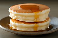 Fluffy stacked pancakes with golden maple syrup dripping down sides on rustic ceramic plate, extreme close up showing soft texture and warm amber tones.