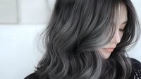 Young Asian woman with trendy silver gray wavy hair style shown in profile against white background, demonstrating modern hair coloring and styling techniques.