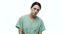 Middle-aged man with dark hair and facial stubble wearing a wrinkled sage green v-neck shirt against white background, suitable for healthcare, medical, or professional portraits.
