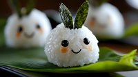 Cute bunny-shaped rice ball with nori ears and kawaii face made from seaweed and carrot on bamboo leaf, creative Japanese food art for children's bento lunch.