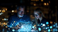 Diverse business team analyzing digital data visualization with glowing blue particles effect at night office, illuminated by laptop screen glow.