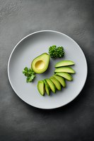 Fresh sliced avocado and parsley arranged on white ceramic plate against dark gray background. Minimalist food styling for healthy eating concept.