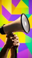 Hand holding a megaphone raised up against a vibrant colorful geometric background, symbolizing announcement, protest, or marketing campaign.