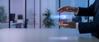 Businessman holding glowing holographic data interface above table in modern office with windows and plants, representing digital technology and business innovation.