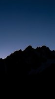 Silhouette of jagged mountain ridge against clear twilight sky, creating dramatic contrast between dark peaks and blue gradient background for nature and landscape designs.