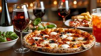 Rustic Italian pizza with pepperoni, melted mozzarella and fresh basil on wooden table with red wine glasses, salad and cocktails in restaurant setting.