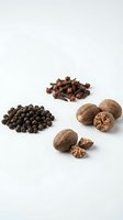 Assorted whole spices and nuts including black peppercorns, cloves, and walnuts arranged on white background for culinary and cooking projects.