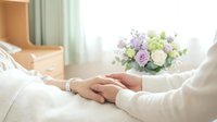 Caregiver gently holding patient hand in hospital room with soft floral bouquet, conveying comfort, support, and compassionate care.