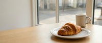 Fresh croissant and coffee cup on wooden table by window in modern cafe interior for breakfast morning routine and bakery business concept.