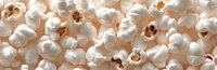 Fresh popcorn kernels scattered in panoramic view showing white fluffy texture and golden centers, creating appetizing snack food background pattern.