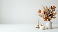 Autumn dried flowers and leaves in white ceramic vase with candle and pumpkin on white surface for fall home decor and seasonal styling.