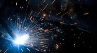 Metal welding process with bright electric arc and flying sparks in industrial workshop environment for manufacturing and construction projects.