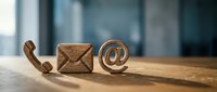 Wooden communication icons including phone, email envelope and at symbol on desk surface representing contact methods and customer service concepts.