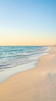 Serene beach scene with gentle waves washing onto golden sand shore under soft pastel sunset sky creating peaceful coastal atmosphere for relaxation and travel.