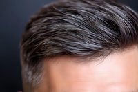 Close-up view of male gray hair against dark background showing natural salt and pepper coloring and modern short hairstyle, highlighting aging process and silver strands.