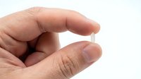 A person's hand holding a small transparent capsule or pill against a white background, suitable for pharmaceutical, healthcare, and medical supplement advertising.
